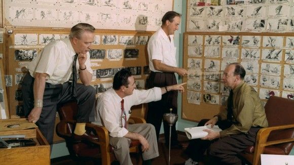 Fyra män diskuterar storyboards på väggar under ett möte för filmproduktion.