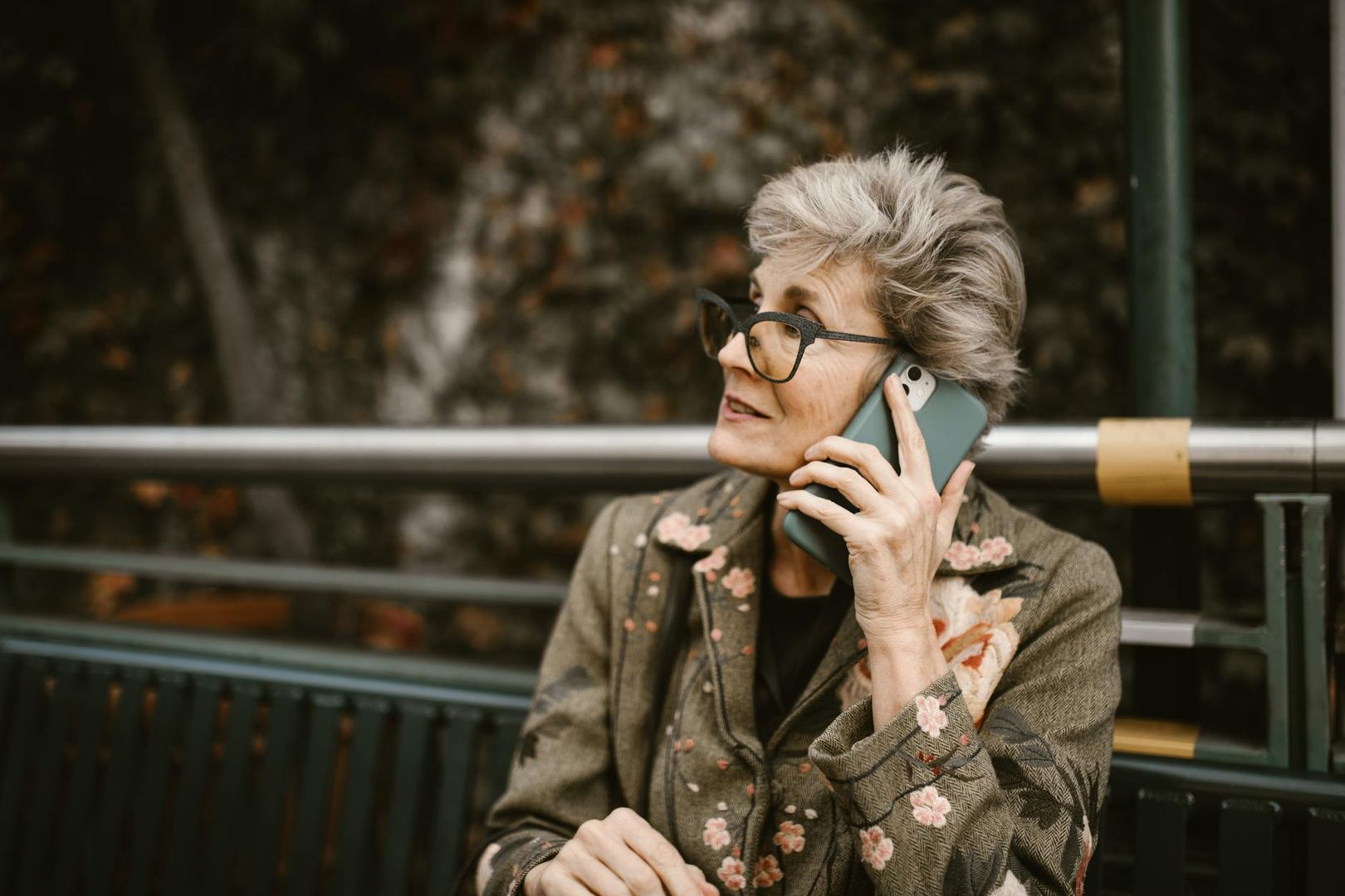 En äldre kvinna med grått hår pratar i sin smartphone utomhus.